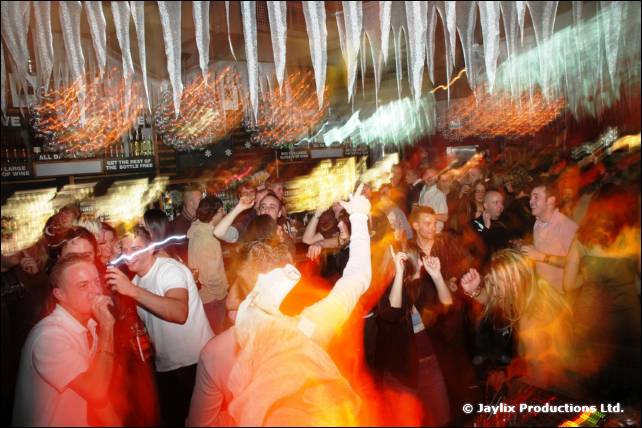 A crowded dance floor in a bar with streaks of orange light and white icicle decorations above
