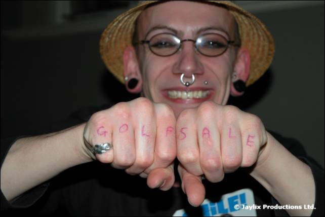 A smiling man in a straw hat and round glasses holds up knuckles with 'Golf Sale' written on them