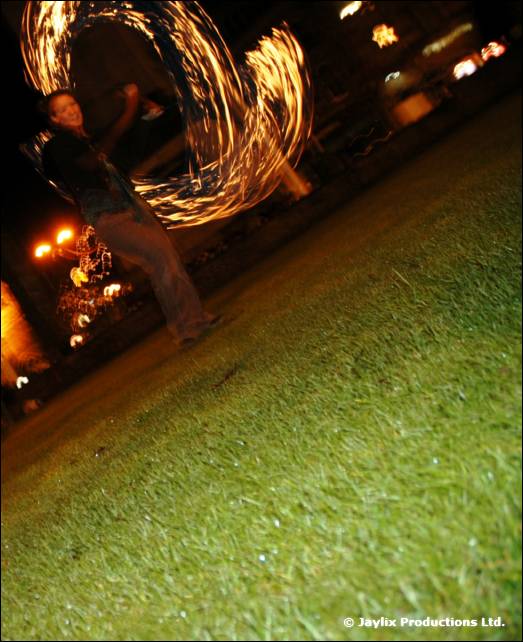 A person spins a trail of fire on a lawn at night, photographed at a tilt