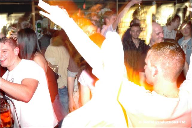 Two men dance in a crowd with raised arms, one in a white top