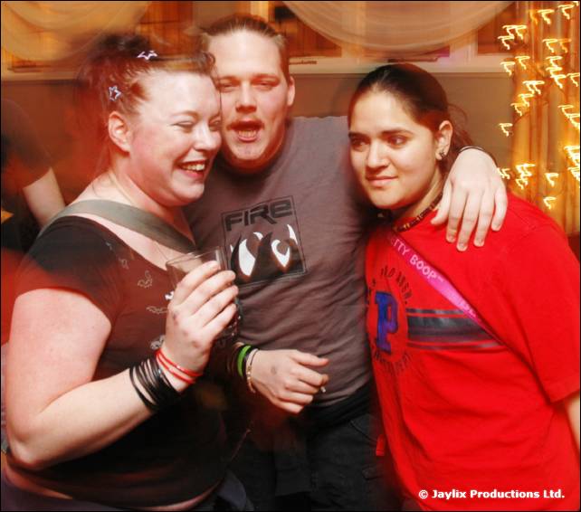 Two women and a man in a grey FIRE T-shirt pose together, one woman in a red top