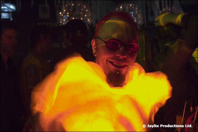 A man with pink-red hair and red glasses smiles behind a glowing yellow blur
