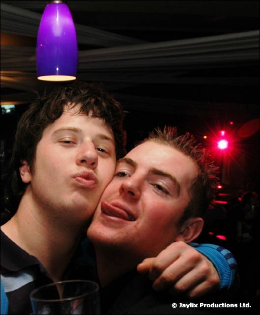 Two young men pull faces, one sticking out his tongue, below a purple light