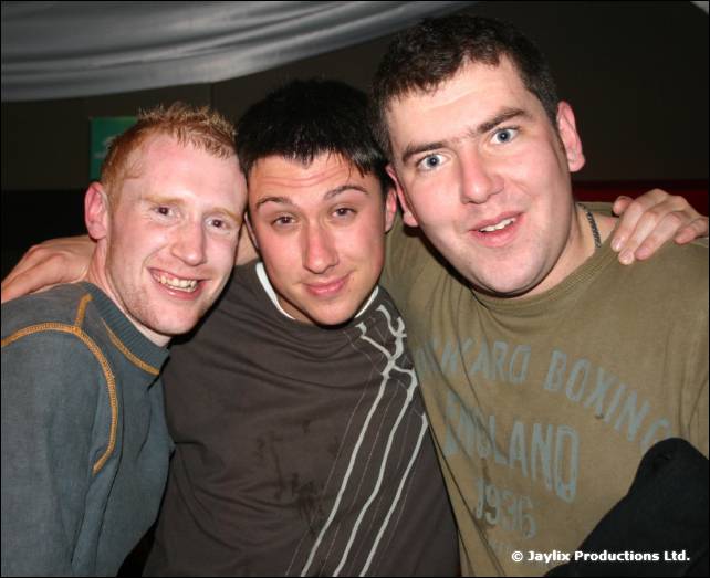 Three men with arms around each other smile at the camera, one in an England boxing T-shirt