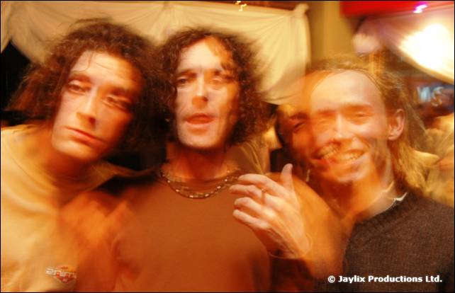 Three men with curly hair pose together in a blur of orange light