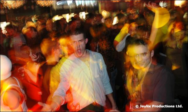 A man in a pale shirt dances in a crowd with blurred figures around him