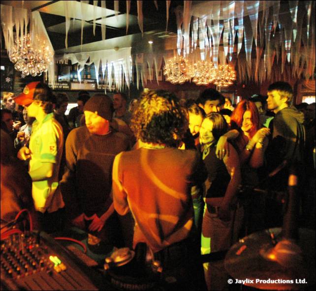 A crowded dance floor seen from behind a DJ mixer, with lights and icicle decorations above