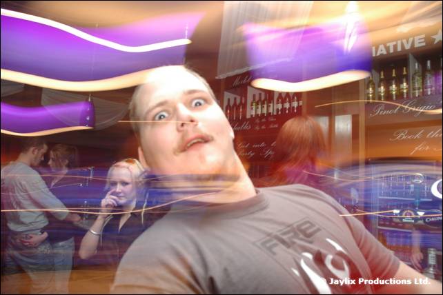 A man in a grey FIRE T-shirt pulls a wide-eyed face in front of purple lights
