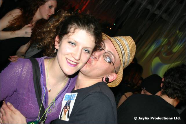 A woman and a man in a straw hat and glasses press their cheeks together
