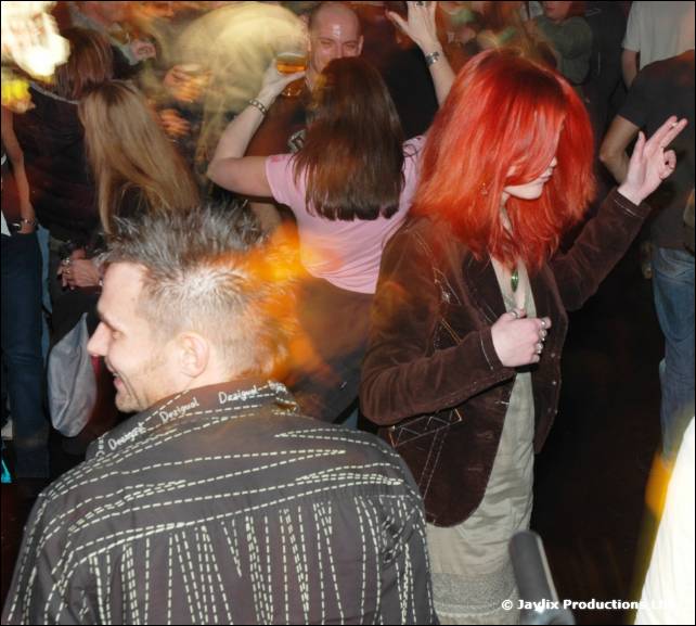 A red-haired woman and a man with spiky hair dance in a crowded room