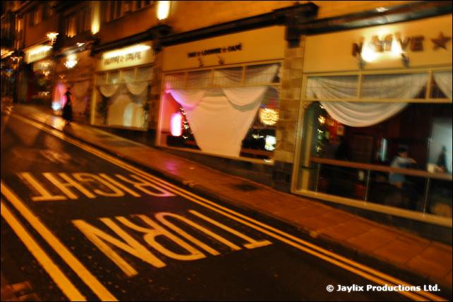 A narrow street at night with TURN RIGHT painted on the road and bars along the pavement