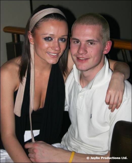 A woman with a headband and a man with short hair smile together with his arm around her