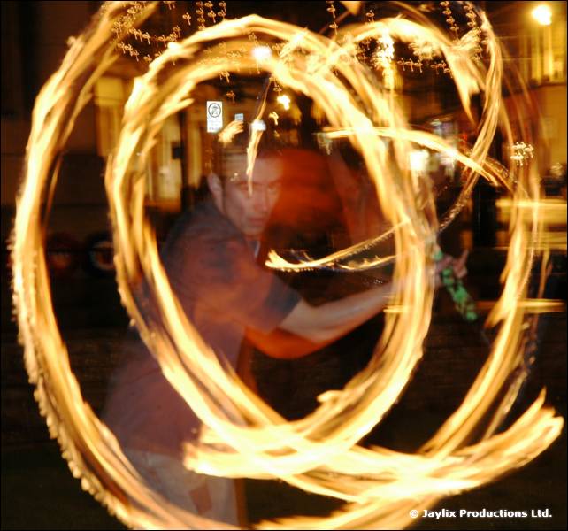 A fire performer swings large circles of flame at night
