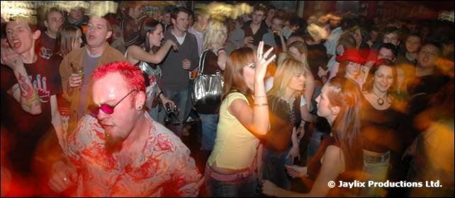 A person with red spiky hair and pink glasses dances in front of a packed crowd