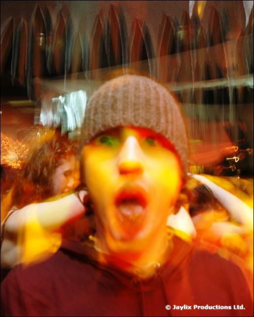 A blurred person in a woollen beanie and red hooded top pulls a surprised face with mouth open