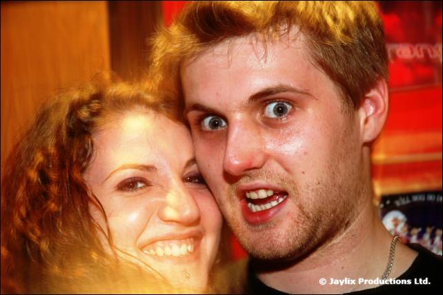 A woman and a man with wide eyes press their faces together and pull expressions at the camera