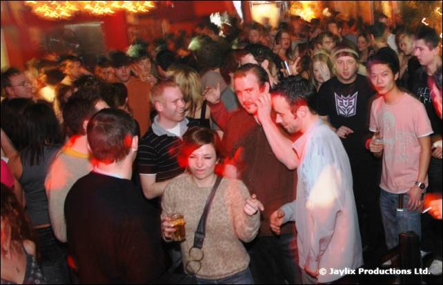 A crowd of people standing and dancing in a busy bar