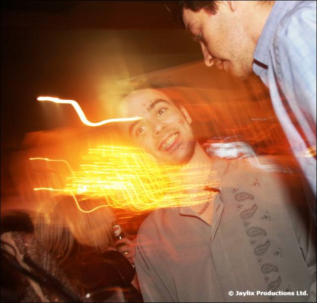 A blurred man smiles up at the camera with light trails across the frame as another man leans over