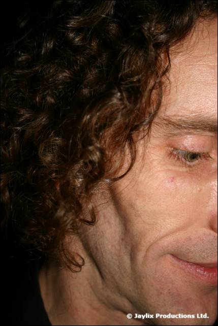 Close-up of the side of a man's face with dark curly hair, eyes looking down