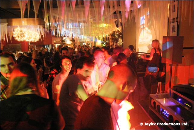 A packed dance floor under white streamers and chandeliers, with people dancing