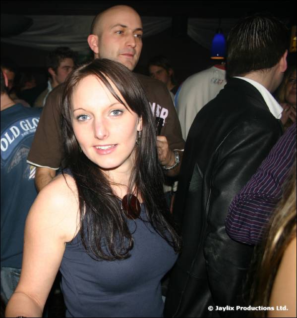 A woman with long dark hair looks at the camera in a crowded room with men standing behind her