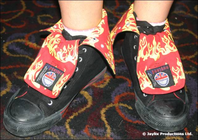 Feet in black trainers wearing red flame patterned shoe covers on a patterned carpet