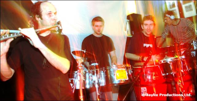 A trumpet player and drummers perform on stage in red light