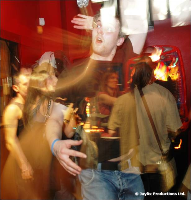 A blurred man dances with an arm out in a red walled bar, people around him