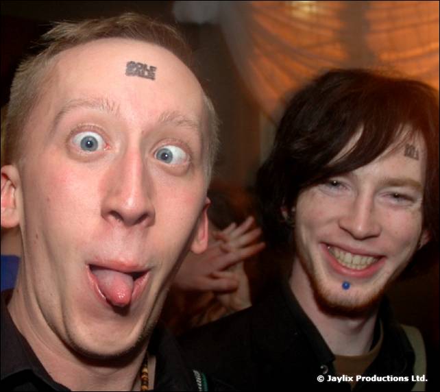 Two men pull faces close to the camera, one with his tongue out and a Golf Sale sticker on his forehead