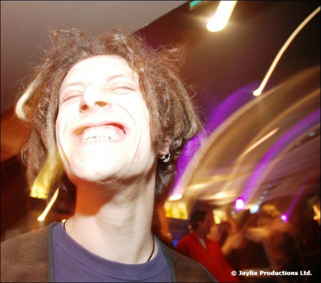 A man with messy hair laughs with eyes closed, with purple and white light streaks behind