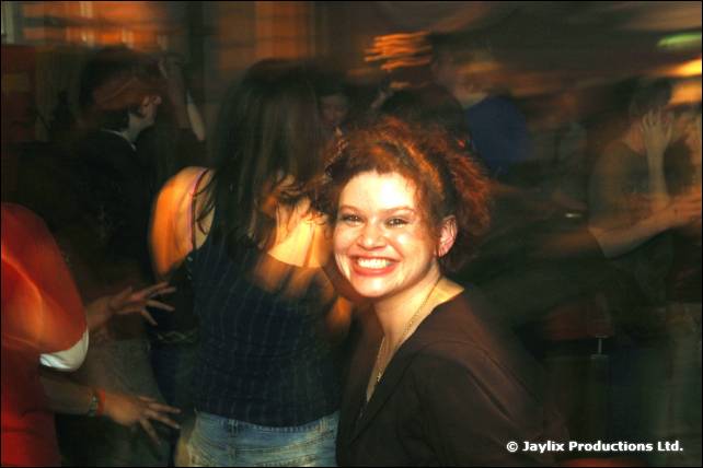 A smiling woman with curly hair stands among blurred dancers