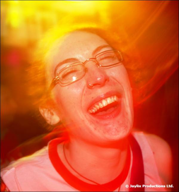 A woman in glasses laughs, lit in strong orange and red