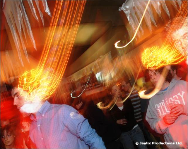 Fire trails swirl around two people dancing under hanging streamers