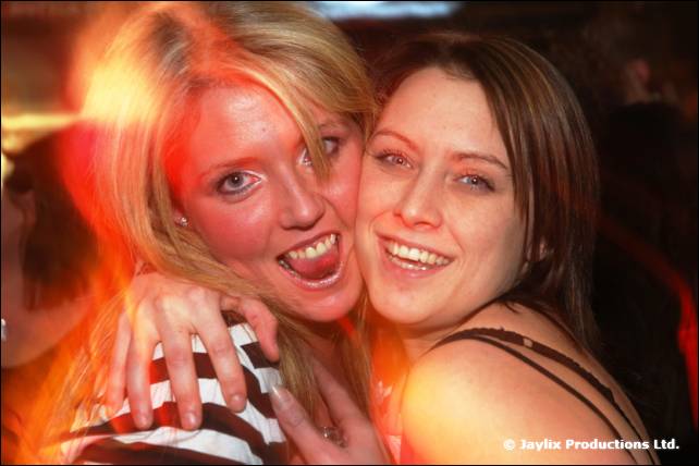 Two smiling women press their cheeks together, one with her mouth open
