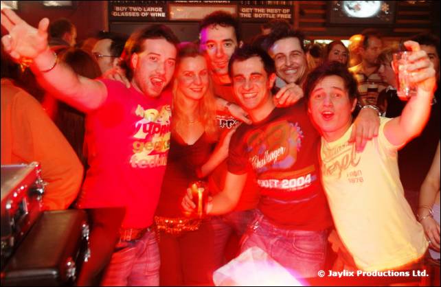 A group of people cheer and pose together in red light, several raising their arms
