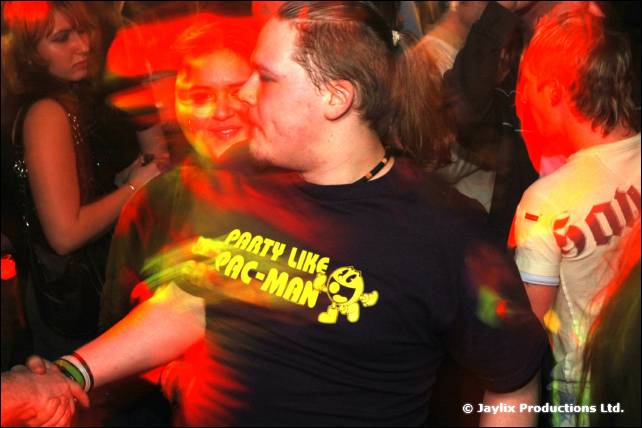 A man in a black Party Like Pac-Man t-shirt dances in a crowd