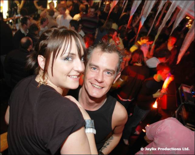 A smiling woman and man pose close together in front of a crowded dance floor
