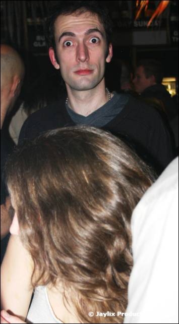 A man with wide eyes looks at the camera, with the back of a woman's head in the foreground
