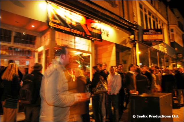 A queue of people outside a lit venue entrance on a street at night