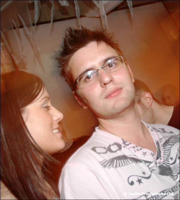 A man with spiky hair and glasses in a white eagle print t-shirt, a woman beside him