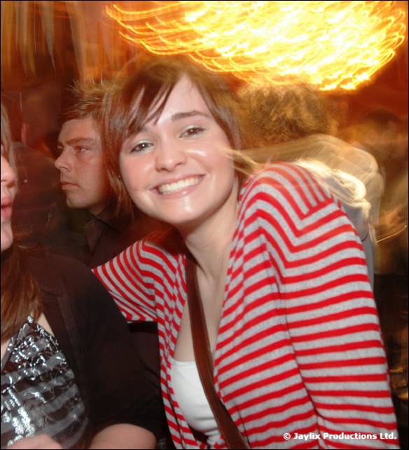 A smiling woman in a red and white striped top stands in a crowd, with light trails above