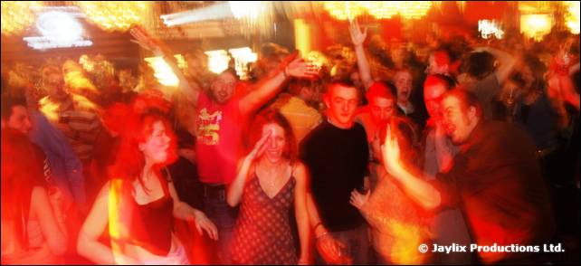 A blurred crowd with raised arms dancing in red light