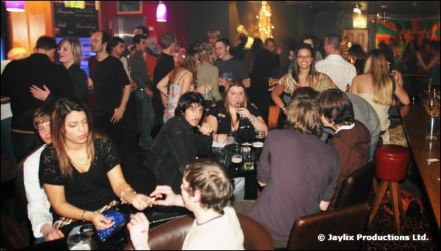 People sit and stand around tables and a bar in a busy venue