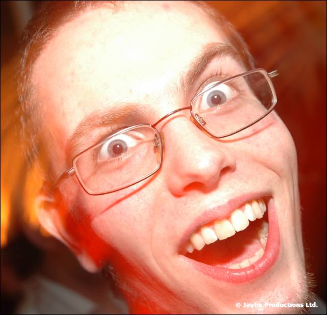 A man in glasses with wide eyes and a big open mouthed grin at the camera