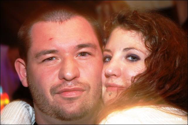 A man with stubble and a woman with curly dark hair press their heads together
