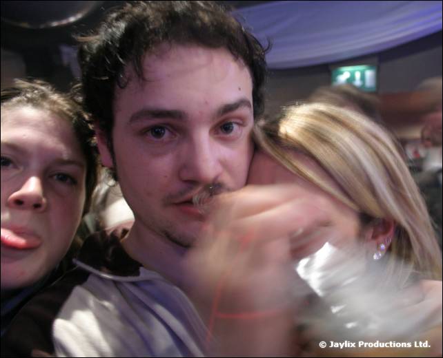 Three people crowd together, one with a tongue out and another hiding his face behind a hand