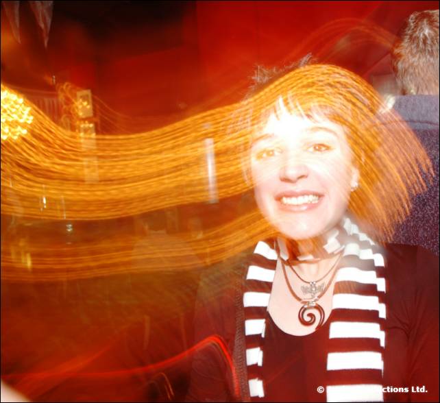 A smiling woman in a black and white striped scarf, with a wide orange light trail across the frame