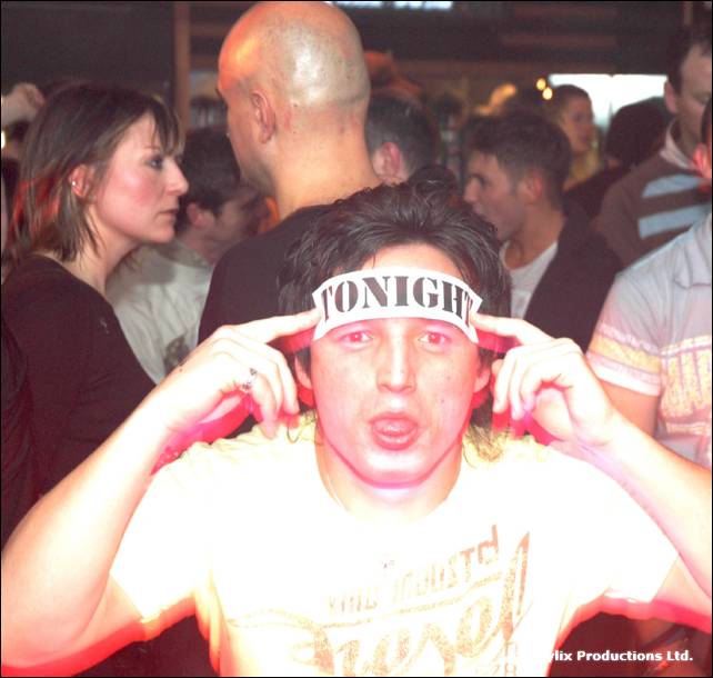 A man holding a white strip of paper that says TONIGHT with both hands at the side of his forehead in a crowd