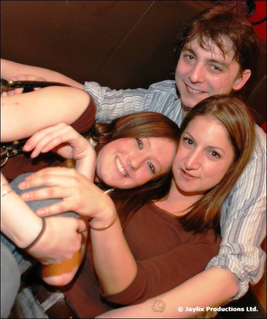 Two women and a man cuddle together on a sofa, smiling