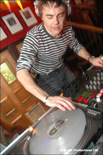 A DJ in a black and white striped top mixes at a turntable